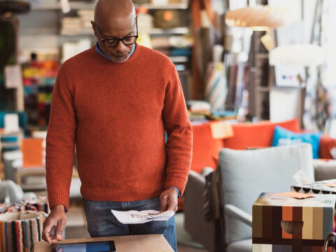 middle-aged man with glasses views uses a tablet to review product information in a modern furniture store