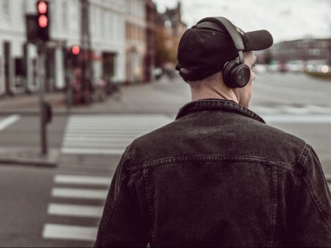 Man with headphones listens to programming while crossing a city street.