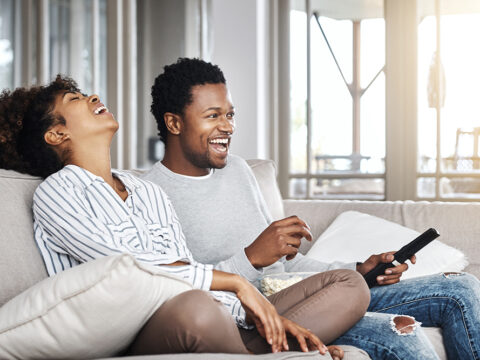 A couple laughing and watching TV which may be powered by advanced TV advertising.