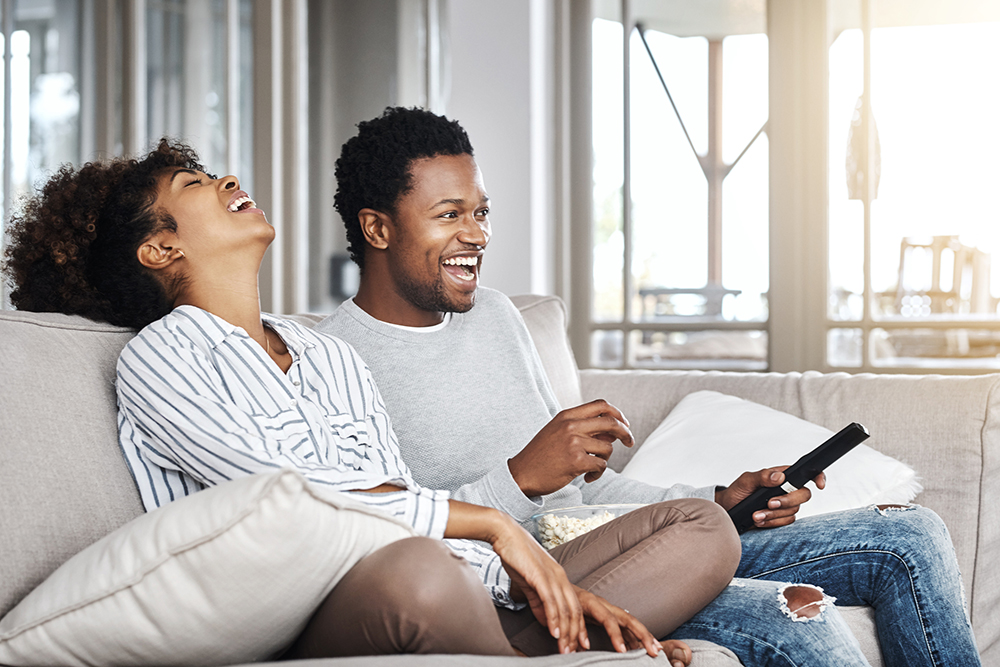 A couple laughing and watching TV which may be powered by advanced TV advertising.