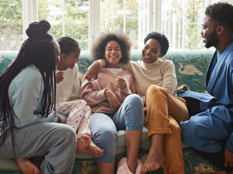 A modern Black/African American family laughts together on the couch