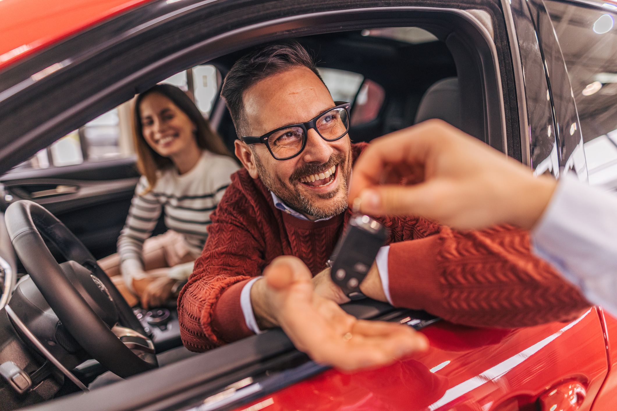 A couple sitting in a car, receiving the keys from a car dealer